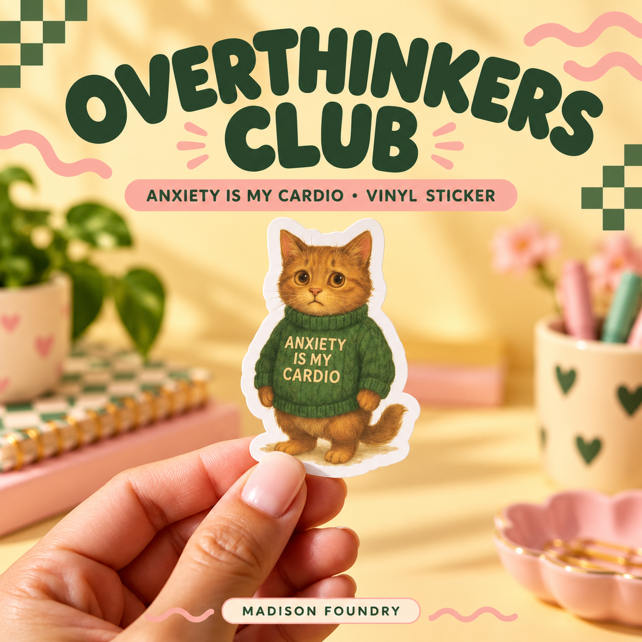 Hand-held Anxiety Is My Cardio orange tabby sticker in a butter-yellow, forest-green and pink Overthinkers Club workspace.