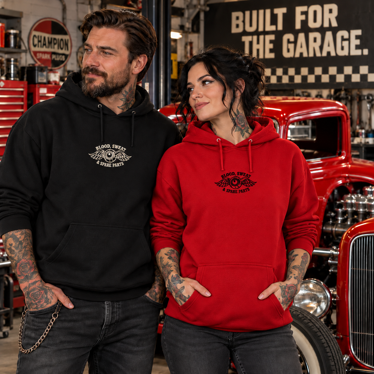 Tattooed models in garage: woman wearing red hoodie with small black embroidery, man wearing black hoodie with cream embroidery