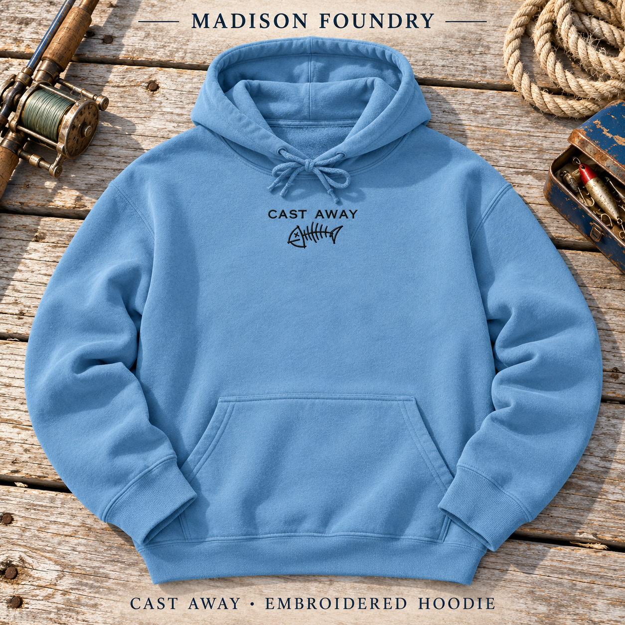 Denim blue Cast Away hoodie with small black fishbone embroidery on a weathered fishing dock