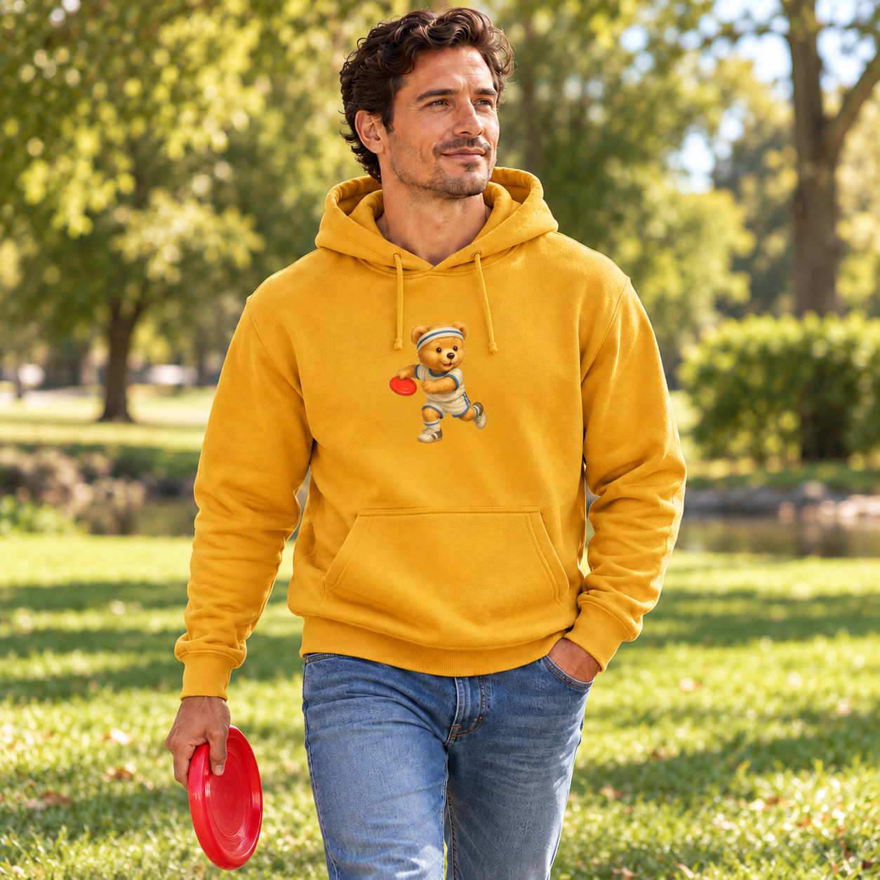 Man wearing gold Frisbee Bear Hoodie carrying red frisbee in park