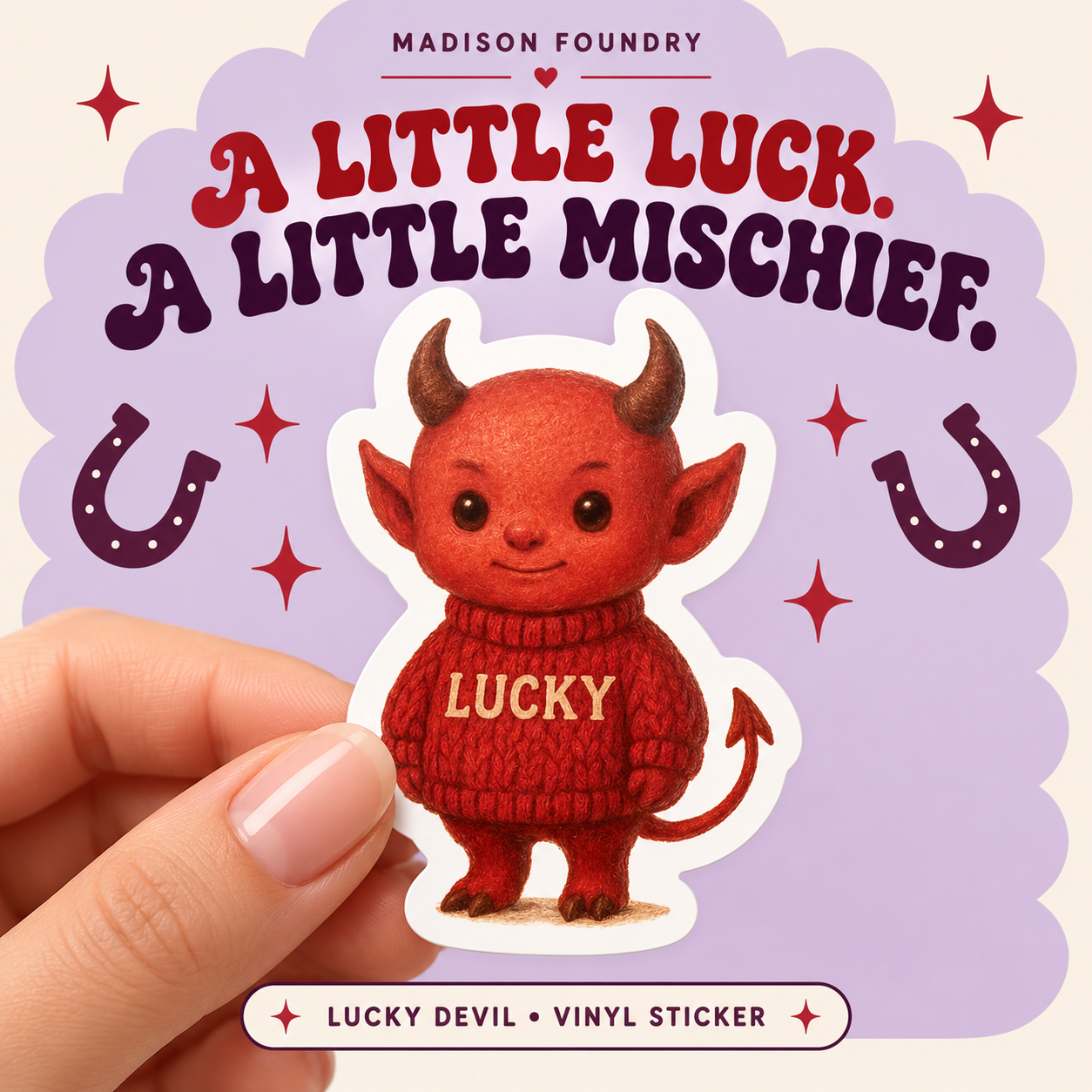 Hand-held Lucky Devil vinyl sticker with red knitted sweater, horns and arrow tail against lilac, cream and cherry red lucky-charm graphics.
