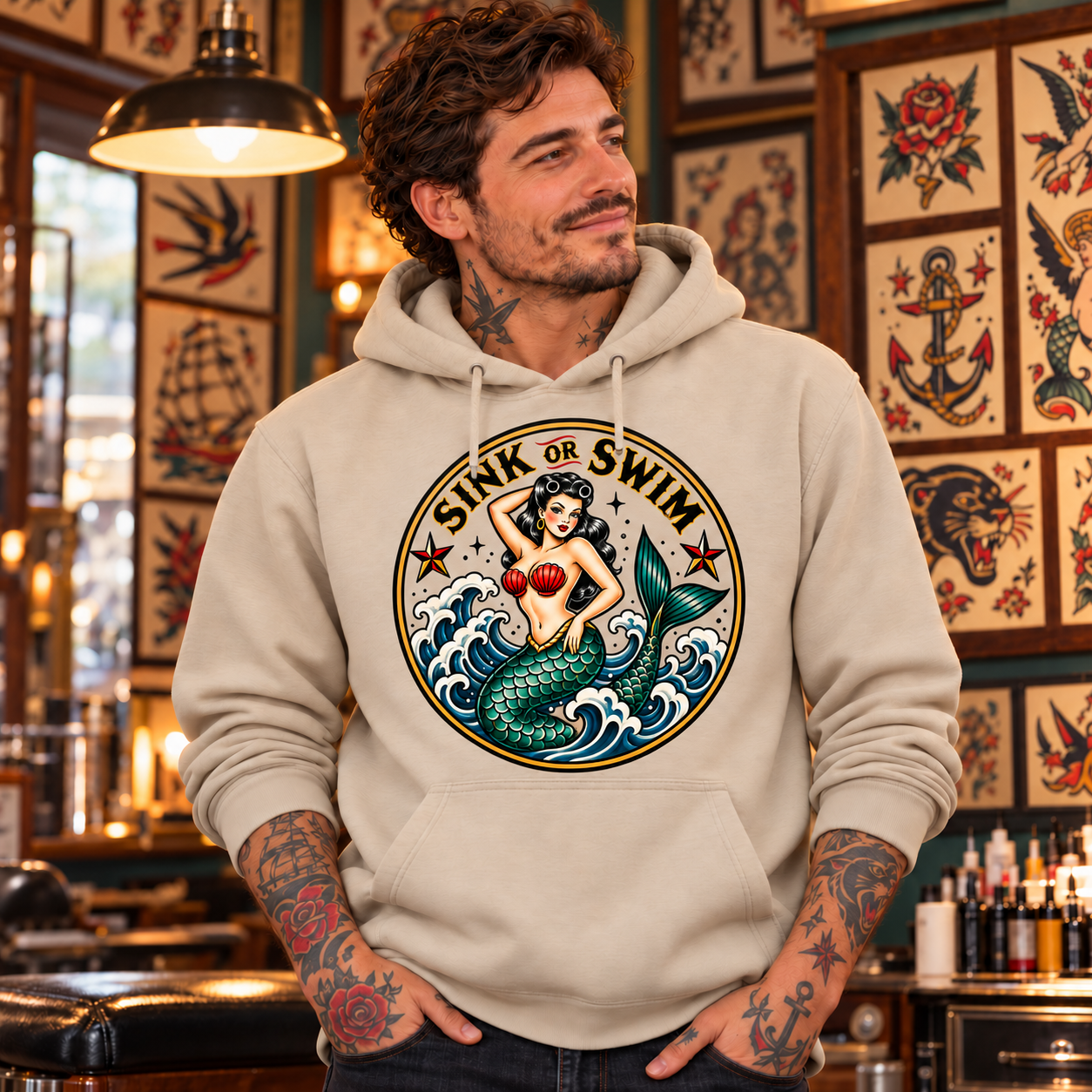 Tattooed man in Sand Sink or Swim hoodie with fabric visible through artwork