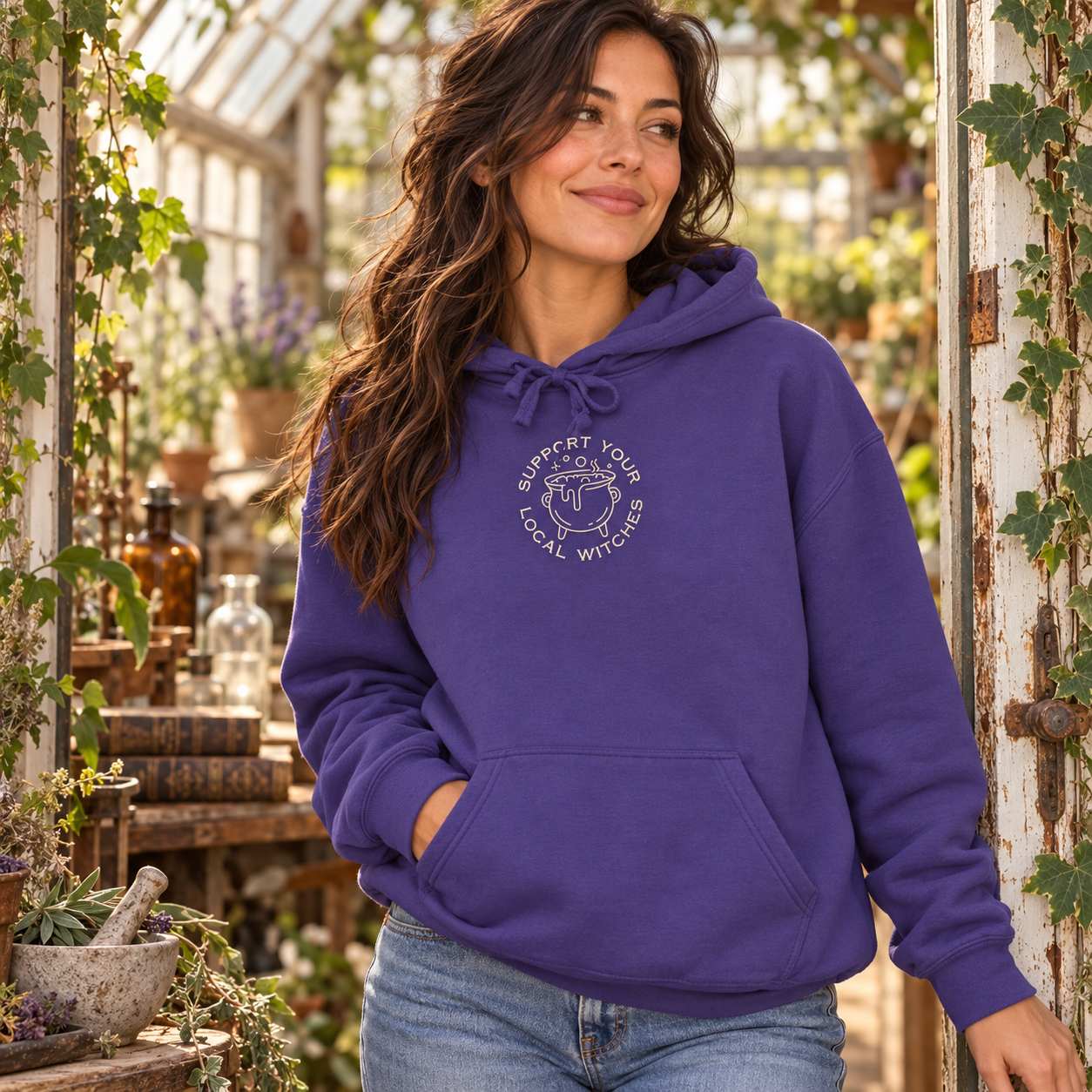 Woman wearing purple hoodie with small vanilla cauldron embroidery in a botanical greenhouse